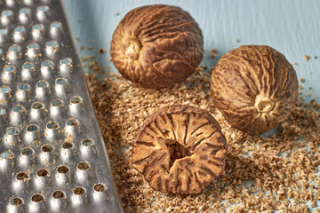 three nutmegs and a metal grater on a blue wooden table