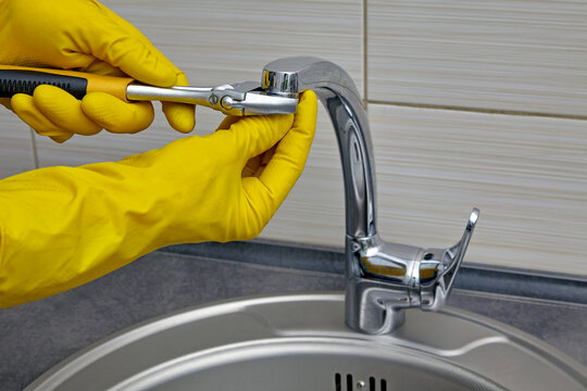 plumber in yellow rubber gloves repairing and servicing a water faucet in a kitchen