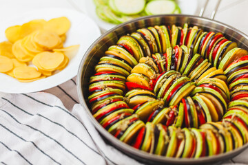 Homemade ratatouille preparation and serving. Child's hands placing vegetable slices into a baking...