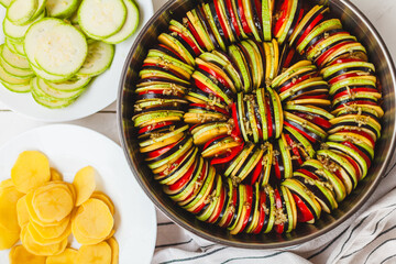 Homemade ratatouille preparation and serving. Child's hands placing vegetable slices into a baking...