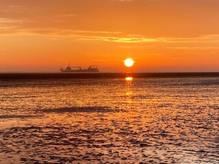 Schiff fährt am Horizont durch Sonnenaufgang am Meer / Cuxhaven an der Nordsee