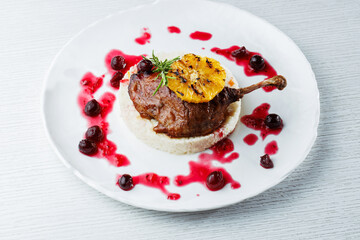 Gourmet duck leg with grilled orange, cherry sauce, and creamy risotto on a white plate. Elegant restaurant-style meal. Top view.