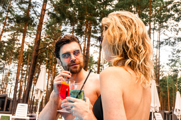 Handsome dark-haired young man in sunglasses and a blonde woman drinking refreshing beverages while...