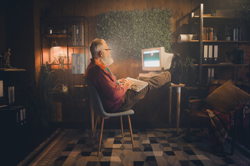 Fototapeta premium Middle-aged man working on an old computer in a cozy home office setting with casual style during the evening