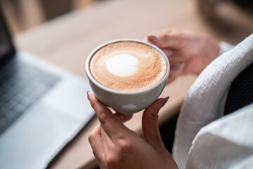 Close-up of hands Holding cup mug of Hot coffee latte wits business female casual working with laptop computer in coffee shop like the background,communication concept