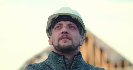 Construction worker in hard hat looking upward confidently, open structure in background,...