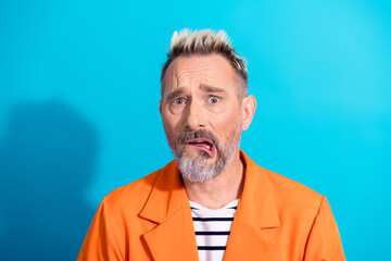 Mature man with dyed blond hair and beard in an orange jacket making a funny facial expression...