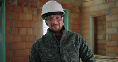 Construction worker holding angle grinder confidently in unfinished building interior, safety gear,...