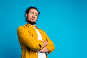 Confident young man in casual yellow shirt posing with expressive attitude and crossed arms against...