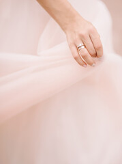 Bride in elegant pink wedding dress holding a veil, marriage concept. Bridal hand with engagement ring close-up