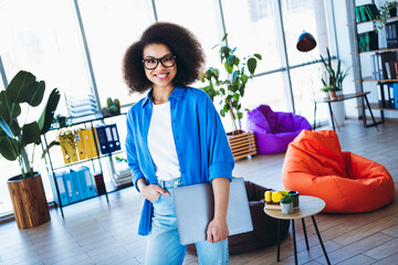 Confident young businesswoman smiling while working in a modern creative office space with colorful...