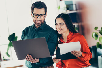 Two professionals collaborating in a modern office while reviewing documents and using a laptop to...