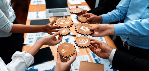 Obraz premium A diverse team collaborates in a meeting room, showcasing wooden gears with business icons. This image portrays strategy, innovation, and effective communication in action. Amity