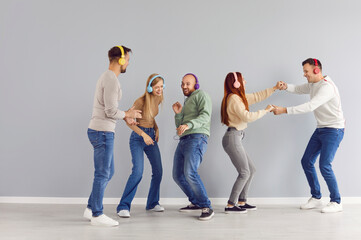 Naklejka premium Happy friends enjoying party, listening to music, dancing and having good time together. Group of young people in colorful stereo headphones dancing by grey wall to playlist of favorite disco songs