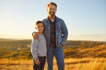 Portrait of a happy smiling parent father hugging his child boy standing in the field in nature and...