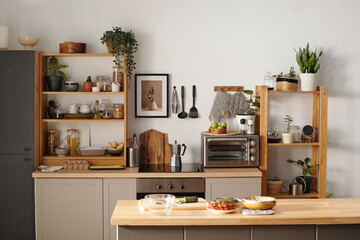 Cozy modern kitchen showcasing wooden shelving filled with plants and kitchenware. Central counter displaying fresh ingredients for culinary preparations