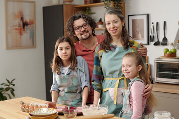 Portrait of multiracial family smiling and baking together in modern kitchen setting. Parents with...
