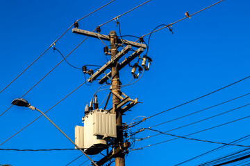 Electric pole with transformer and overhead wires under clear blue sky in Brazil. This image...