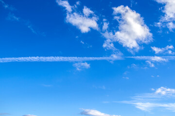 Vibrant blue sky with white clouds and contrail. Ideal for weather, travel, environment, or...