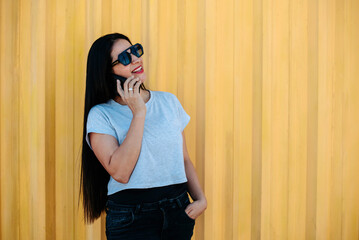 Confident woman smiling and talking on smartphone against a bright yellow wall. Stylish communication concept.