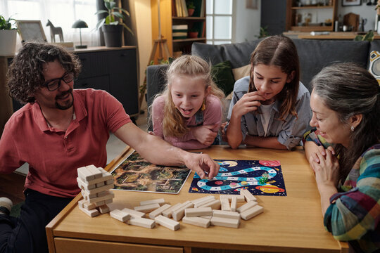 Family sitting at table playing board game, with three children and two adults concentrating on the game, socializing and enjoying bonding moment
