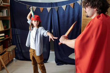 Child and adult engaging in theatrical role-playing wearing colorful costumes in a home setting. Room decorated with a blue curtain backdrop and string of flags