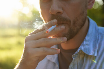 Man smoking cigarette outdoors on sunny day, closeup