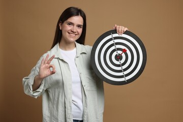Targeting. Smiling woman with dart board and arrow showing ok gesture on beige background