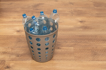 A recycling container sits on a wooden floor, filled with clear plastic bottles awaiting proper...