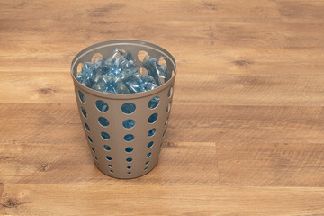 A container filled with sorted recyclable materials is placed on a wooden floor. The arrangement...