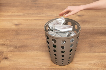 A hand places aluminum cans into a recycling bin made for sorting waste. The setting features a...
