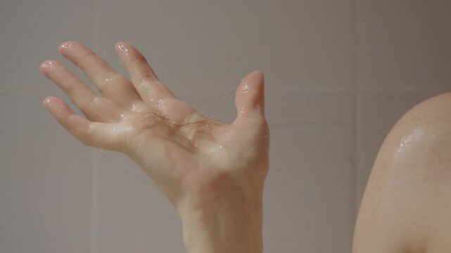 A woman is in the shower using body foam and shampoo while experiencing noticeable hair loss. She gently washes her hair as strands fall during the process.