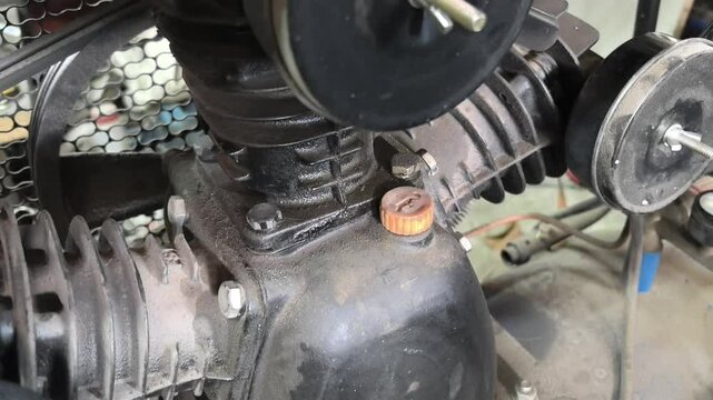 This clip highlights crucial maintenance being performed on a small air compressor in a garage, showcasing the engine's condition and key components for efficient operation.