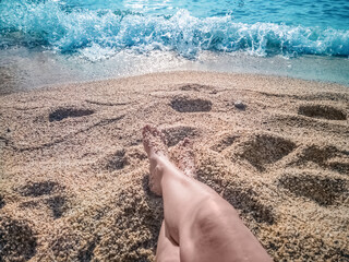 Relaxing moment on a sandy beach in Alanya, Turkey, with legs resting near the shoreline. Gentle waves crash softly onto the shore, creating a peaceful and calming atmosphere by the Mediterranean Sea