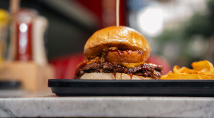 Gourmet Smash Burger with Onion Rings and BBQ Sauce Served with Fries Outdoors