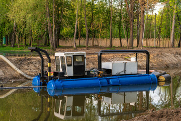 Dredge machine anchored in canal with vegetation in the background, blue pontoons and white cab structure