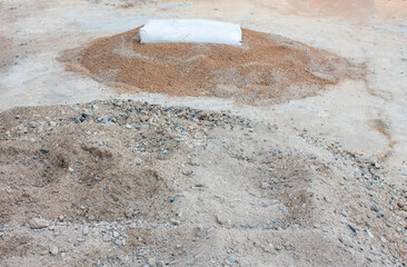 There is construction sand on the ground, and on top of it there is a bag of cement for preparing mortar for laying bricks.