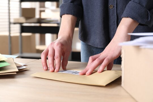 Woman putting barcode onto envelope at table in post office, closeup