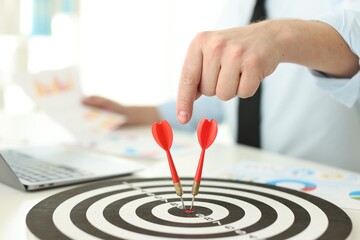 Man pointing at dartboard while working at table indoors, closeup