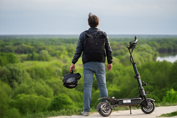 Man riding electric scooter standing on hill enjoying nature, beautiful green forest landscape