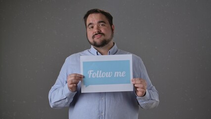 Man Holding Follow Me Sign on Gray Background