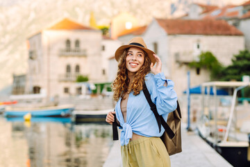 Beautiful female traveler in a hat and with a backpack enjoying the seascape at sunset. Young woman...