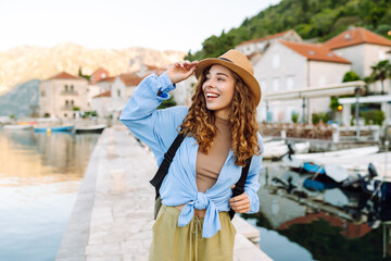 Beautiful female traveler in a hat and with a backpack enjoying the seascape at sunset. Young woman...