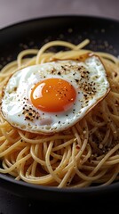 Delicious close-up of spaghetti topped with a sunny-side-up egg, seasoned with black pepper and spices, served on a black plate for a cozy comfort food dining experience.

