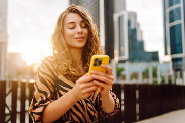 Happy woman in dress and holding a phone in her hands walks along the city street. Young tourist...
