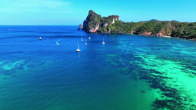 Aerial Shot Of Motorboats Moving On Rippled Sea Water By Rock Formation Against Clear Sky, Drone Flying Forward During Sunny Day - Phi Phi Islands, Thailand