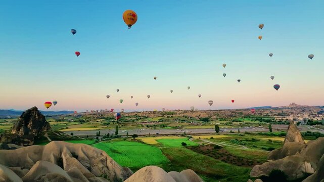 Goreme, Turkey, May 7, 2024: Colorful balloons in Cappadocia fly in the sky over deep canyons at dawn. A lot of balloons with tourists hover and fly in the blue sky above the valley of rocks. 4К