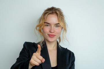 Confident young businesswoman smiling and pointing away while engaging with camera, professional portrait against clean white background