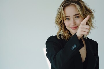 Fototapeta premium Confident young businesswoman smiling and pointing away while engaging with camera, professional portrait against clean white background