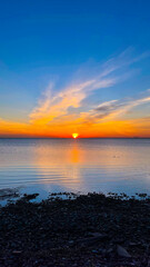 Bright sunset with yellow sun under water surface. Tranquil sunset over the sea. Summer evening. Vertical photography.